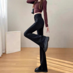 Person in maroon cropped top and black flared jeans dancing in minimalist indoor setting.